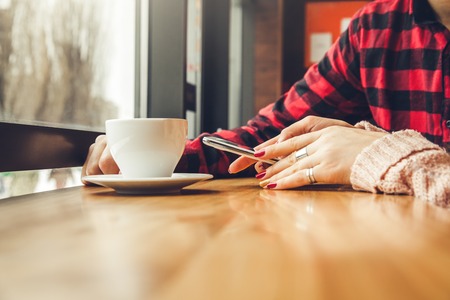 Young couple enjoys coffee in the cafe while using a smartphone in front of the windowの写真素材