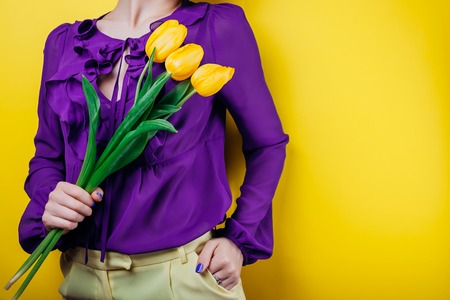 Studio shot of a woman wearing spring outfit and holding yellow tulipsの写真素材