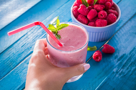 Woman holds smoothie with raspberry on blue tableの写真素材