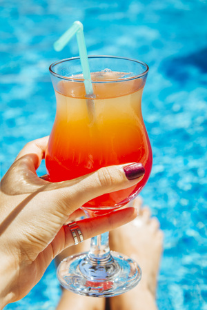 Woman holds a layered cocktail on swimming pool backgroundの写真素材