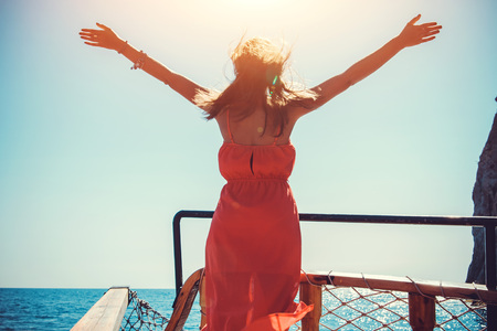 Young woman enjoying the freedom on a wooden yacht while sailing. Model raised her arms against the wind.の写真素材