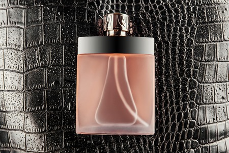 Luxurious bottle of perfume on black crocodile skin texture covered with water dropsの写真素材