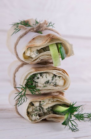 Tortilla wraps with cottage cheese, dill and cucumber on wooden background. Vegetarian food concept....