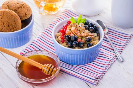 Oatmeal porridge with berries, tea and cookies for breakfast on wooden table. Vegetarian food