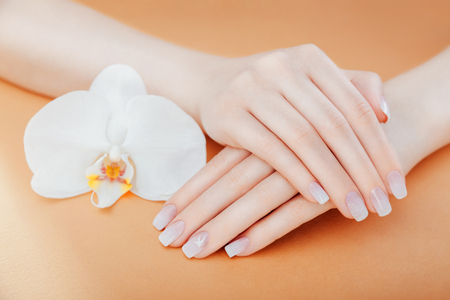 Ombre french manicure with sparkles and orchid on orange background. Female hands with white ombre french manicure and painting. Body care. Beauty conceptの写真素材