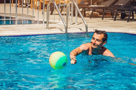 Young man playing water polo in swimming pool of hotel. Water sports. Healthy lifestyle concept. Summer vacation.の写真素材