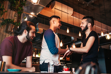 Multiracial young men meeting their friend in lounge bar. Real emotions of best friends happy to see each other. Friendshipの写真素材