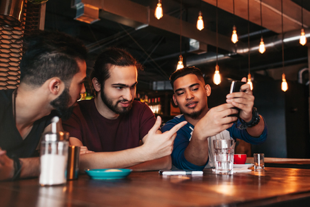 Group of mixed race young men talking in lounge bar. Multiracial friends having fun in cafeの写真素材