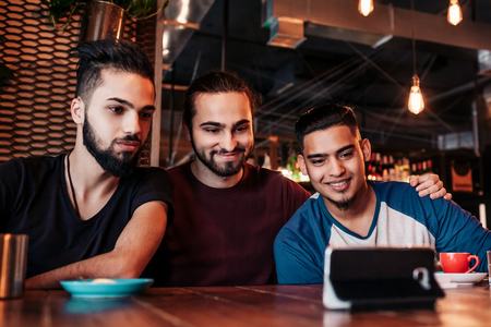Group of arabian friends taking selfie in lounge bar. Mixed race young men having fun in loft cafe. Hipsters hangout togetherの写真素材