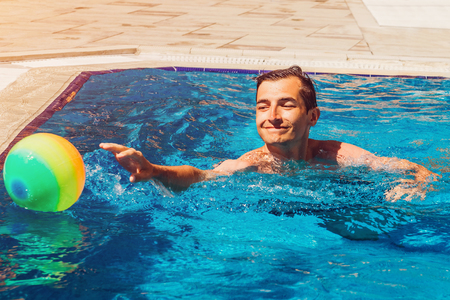 Young man playing water polo in swimming pool of hotel. Water sports. Healthy lifestyle concept. Summer vacation. Summer entertainmentの写真素材