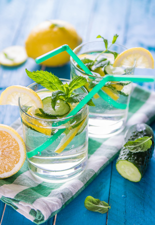 Refreshing lemonade of lemon, cucumber, lime and mint on blue background. Summer drink. Healthy organic drinksの写真素材