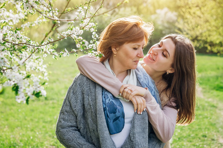 Middle-aged mother and her daughter hugging in blooming spring garden. Mother's day concept. Family valuesの写真素材