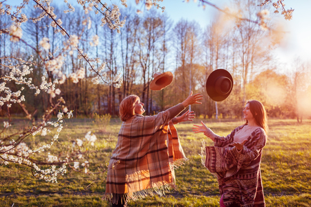 Happy senior mother and her adult daughter throwing hats in spring garden at sunset. Mother's day concept. Women having funの写真素材