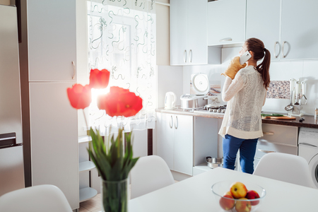 Woman cooking dinner in new kitchen and talking on the phone. Modern kitchen design. White and grey clean dining roomの写真素材