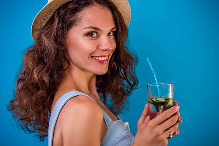 Young woman drinking lemonade on blue background. Happy girl wearing summer outfit. Summer exotic drinksの写真素材