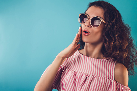 Portrait of a surprised young woman wearing sunglasses on blue background. Excited girl screaming. Stylish summer outfit. Fashionの写真素材