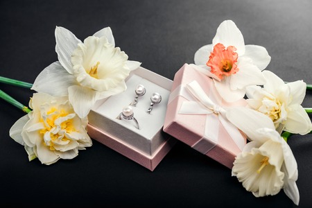 Set of pearl jewellery in gift box with flowers on black background. Silver earrings and ring with pearls as a present for Mother's day. Accessories and jewelry.の写真素材
