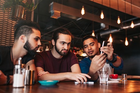 Group of mixed race young men talking in lounge bar. Multiracial friends having fun in cafe drinking coffee. Guys hanging outの写真素材