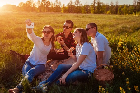 Friends eating pizza outside and having fun. Women and men having picnic at sunset. Young people hanging together. Fast food concept.の写真素材
