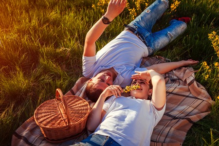 Young couple in love relaxing after having picnic. Woman and man lying on grass and talking at sunset. Guys chilling out.の写真素材