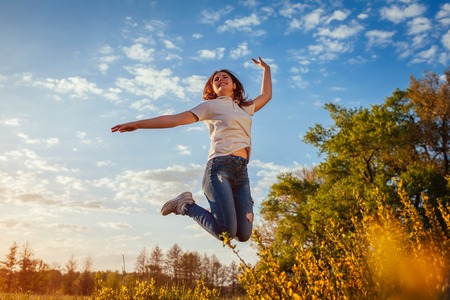 Young woman jumping and having fun in spring field at sunset. Happy and free girl enjoys nature and lifeの写真素材