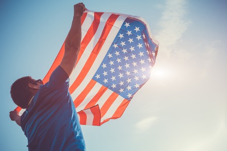 Man holding national USA flag against the blue sky. Celebrating Independence Day of America. July 4thの写真素材