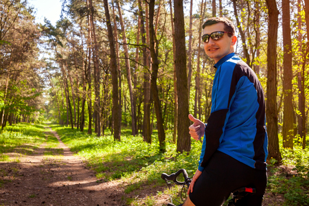 Happy young man bicyclist riding a road bike in spring forest in the morning. Man showing hand with thumb up. Active and healthy way of life concept.の写真素材