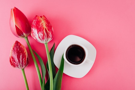 Cup of esspresso coffee and fresh tulips on pink background. Good morning. Inspiration for a new dayの写真素材