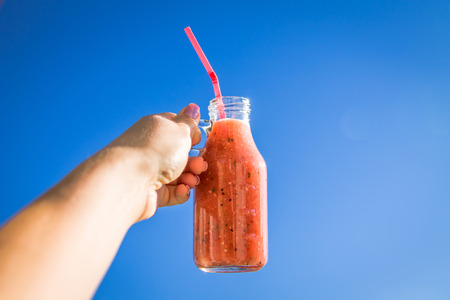 Woman holds a bottle of smoothie against the blue sky. Healthy breakfast. New day with beginning. Dietingの写真素材