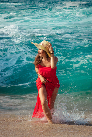 Beautiful woman in red dress runs away from waves on the beachの写真素材