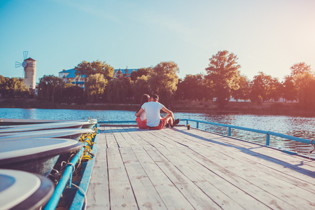Happy couple in love hugging on the river dock at sunset. Young people chilling by water enjoying viewの写真素材