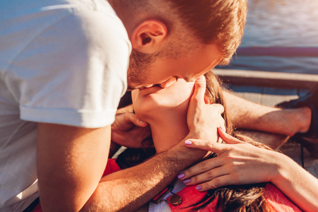 Happy couple in love hugging and kissing by the river at sunset. Romantic date of young studentsの写真素材