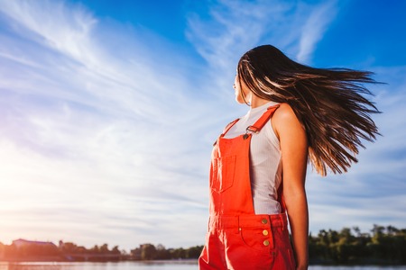 Happy and free young woman on blue sky background enjoying life. Girl chilling on river at sunsetの写真素材