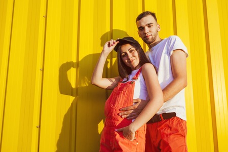 Happy couple in love hugging against yellow wall at sunset. Young hipsters smiling. Spaceの写真素材
