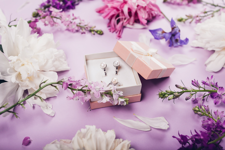 Set of pearl jewellery in gift box with flowers on purple background. Silver earrings and ring as a present. Accessories and jewelry with gems. Stylish jewelleryの写真素材