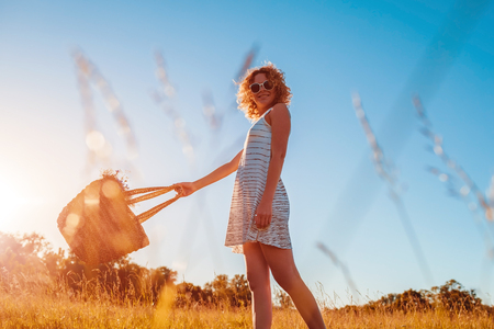Outdoor portrait of beautiful young woman with red curly hair holding bag with flowers. Summer modern lookの写真素材