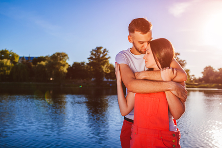 Happy couple in love hugging and smiling by the river at sunset. Romantic summer date. People enjoying lifeの写真素材