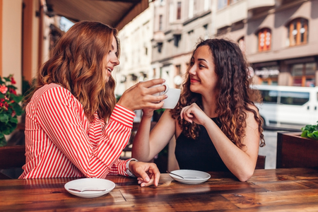 Happy female friends having coffee in outdoor cafe in summer on the street. Women chatting and chilling. Cheersの写真素材