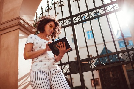 Beautiful college girl reading a book outdoors. Teenager student learning in the yard of universityの写真素材
