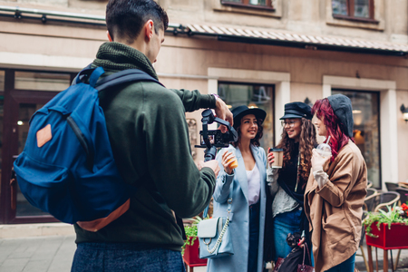 Videographer filming models on city street. Man using steadicam and camera to make footage. Digital devices for video shootの写真素材