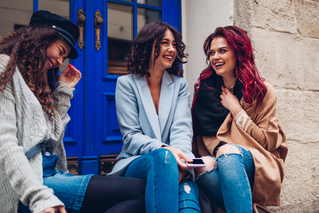 Outdoor shot of three young women chatting and laughing on city street. Best friends talking and...