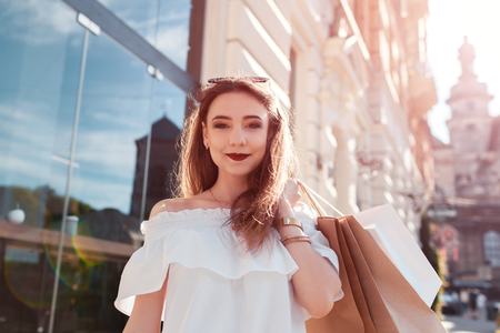 Beautiful stylish young woman with shopping bags walking on city street in summer. Happy girl holding purchases. Shopping center salesの写真素材