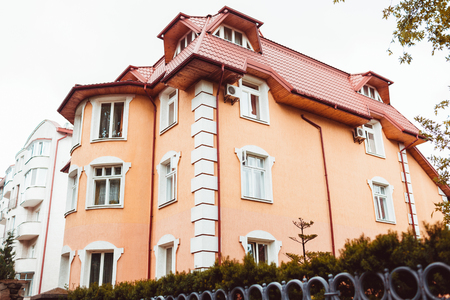 The new multi-storey residential building with green area surrounded with fence. Cozy orange house with red roofの写真素材