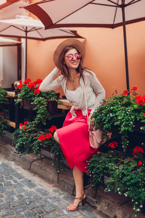 Young woman wearing stylish clothing, jewellery and accessories outdoors. Model standing by cafe with flowers. Beauty fashion conceptの写真素材