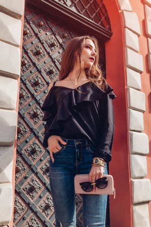 Outdoor portrait of a beautiful stylish woman in sunglasses on city street. Fashion model wearing summer clothing and accessories. Lady holding a handbagの写真素材