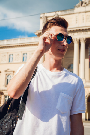Handsome college man checking his glasses against the university. Happy guy student with backpack smilingの写真素材