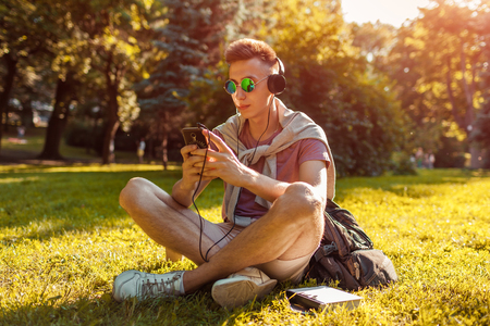 Handsome college man hanging in smartphone and listening to the music in campus park. Happy guy student relaxingの写真素材
