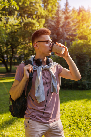 Handsome college guy chilling in spring campus park. Happy man student drinking coffeeの写真素材