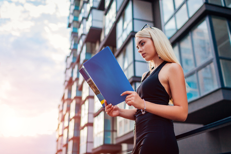 A young female blonde real estate agent reading a contract in front of a modern building in the city.の写真素材