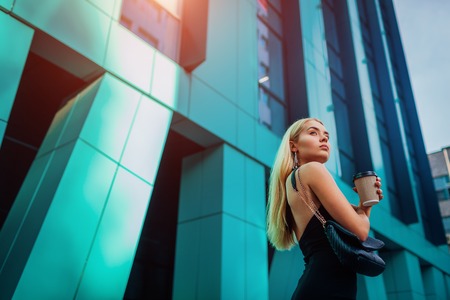 Young blonde businesswoman having coffe break by modern business center in city. Portrait of stylish successful womanの写真素材